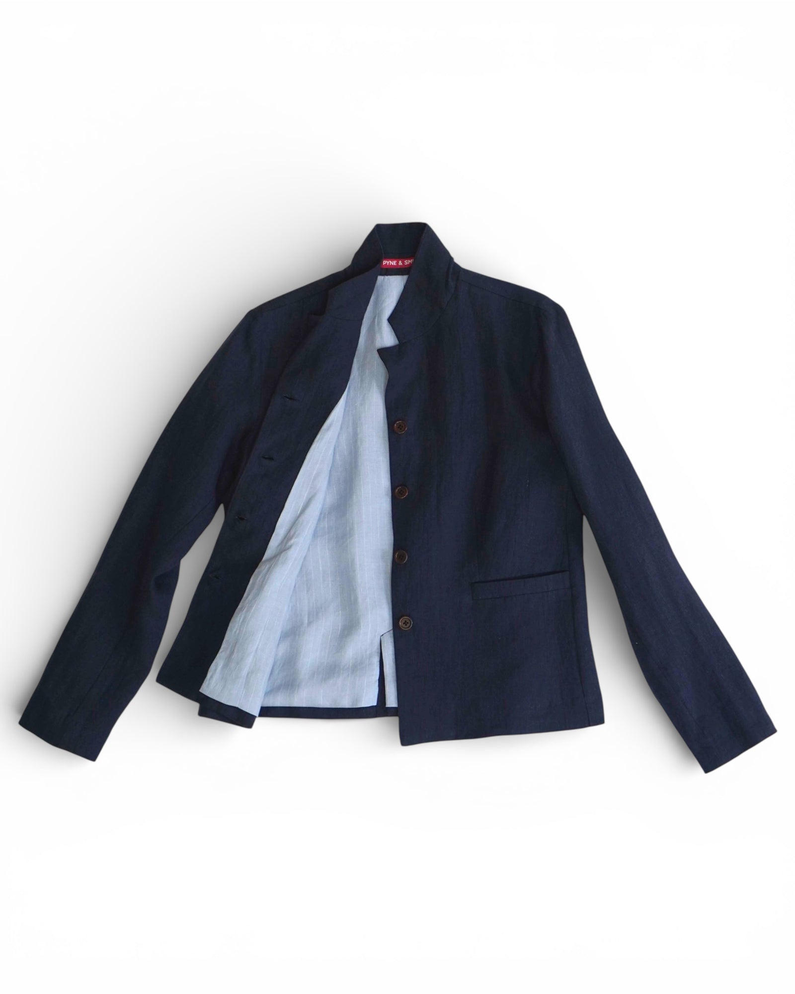 The Tailored Linen Jacket No.10 in Mariner Blue by Pyne and Smith Clothiers, featuring a mandarin collar, brown buttons, and a single chest pocket, is shown flat with its light inner lining partially visible.