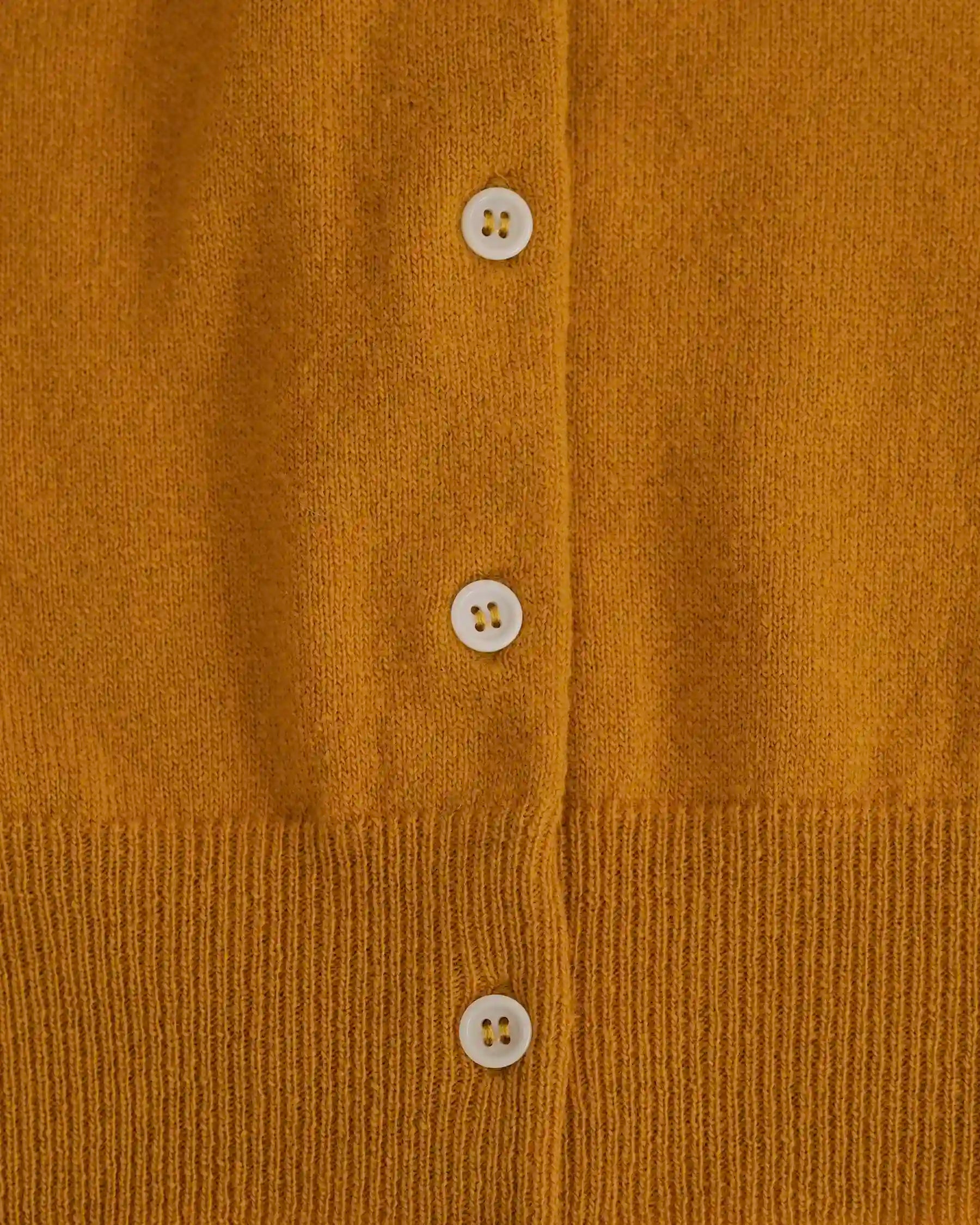 Close-up of the Pyne and Smith Clothiers Merino Cardigan in Coleman's Yellow, featuring a vertical row of four white buttons and ribbed detailing at the hem.