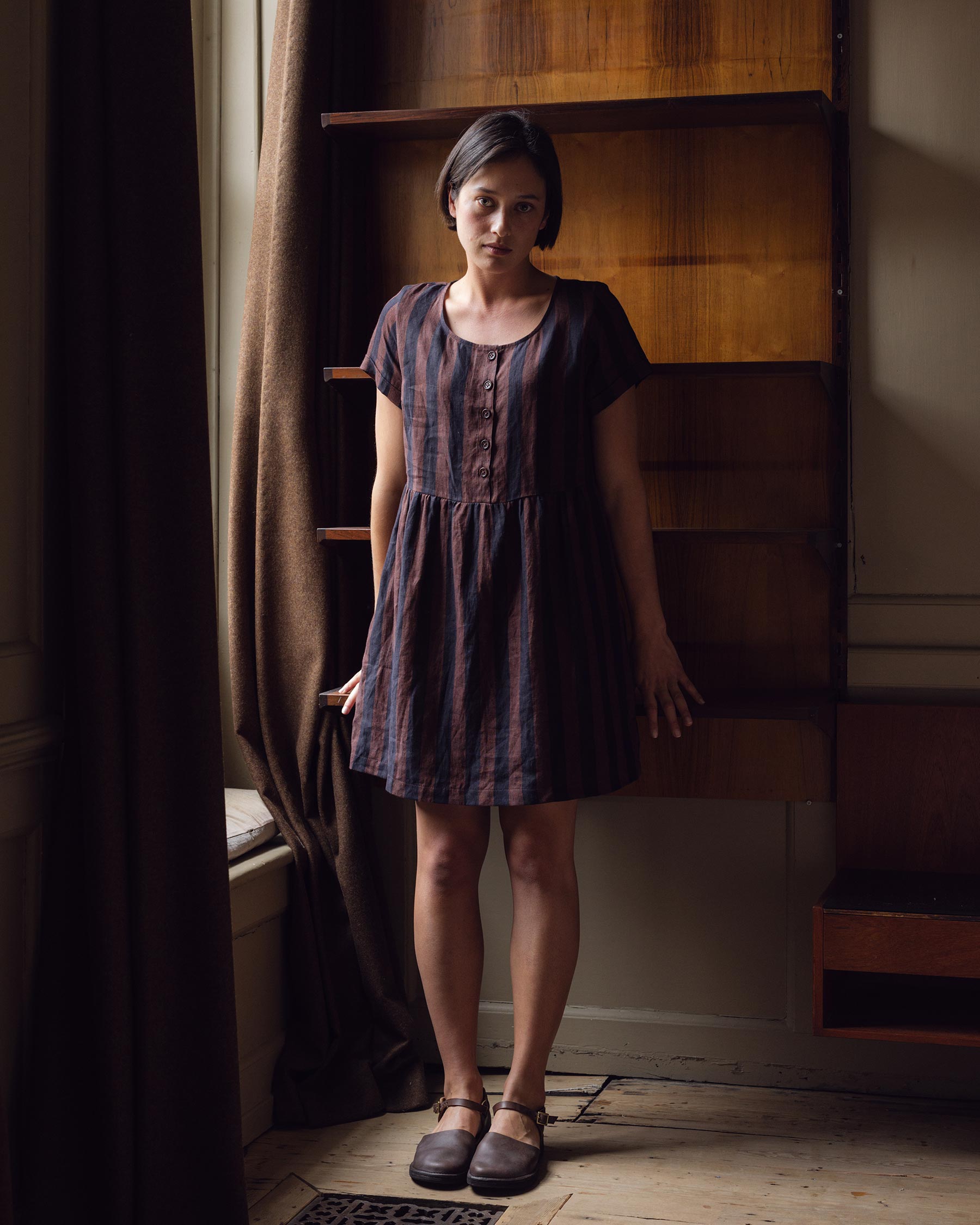 Model wearing button up linen dress in cocoa and black stripe