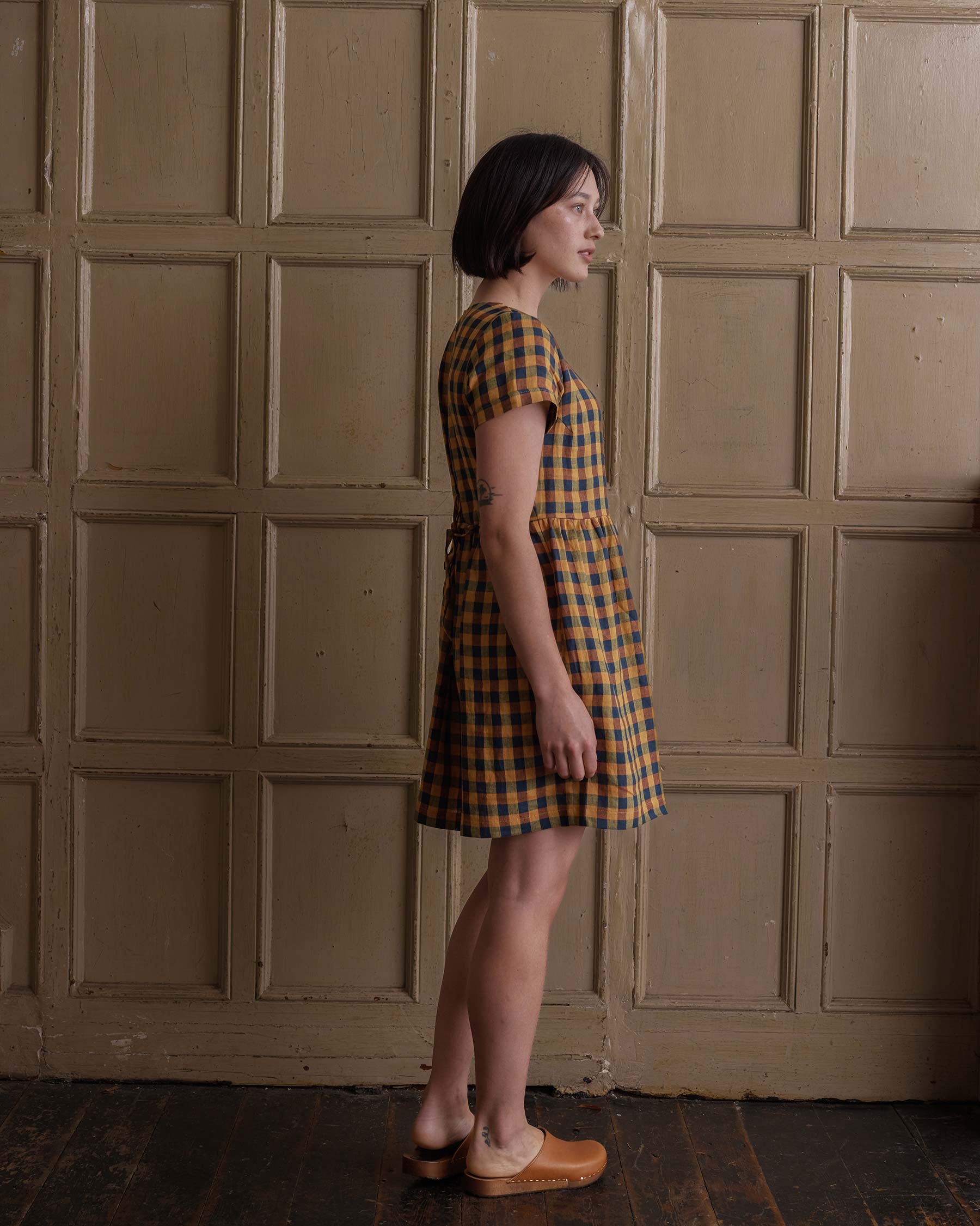 Side view of model wearing button up linen knee length dress in Basque Check