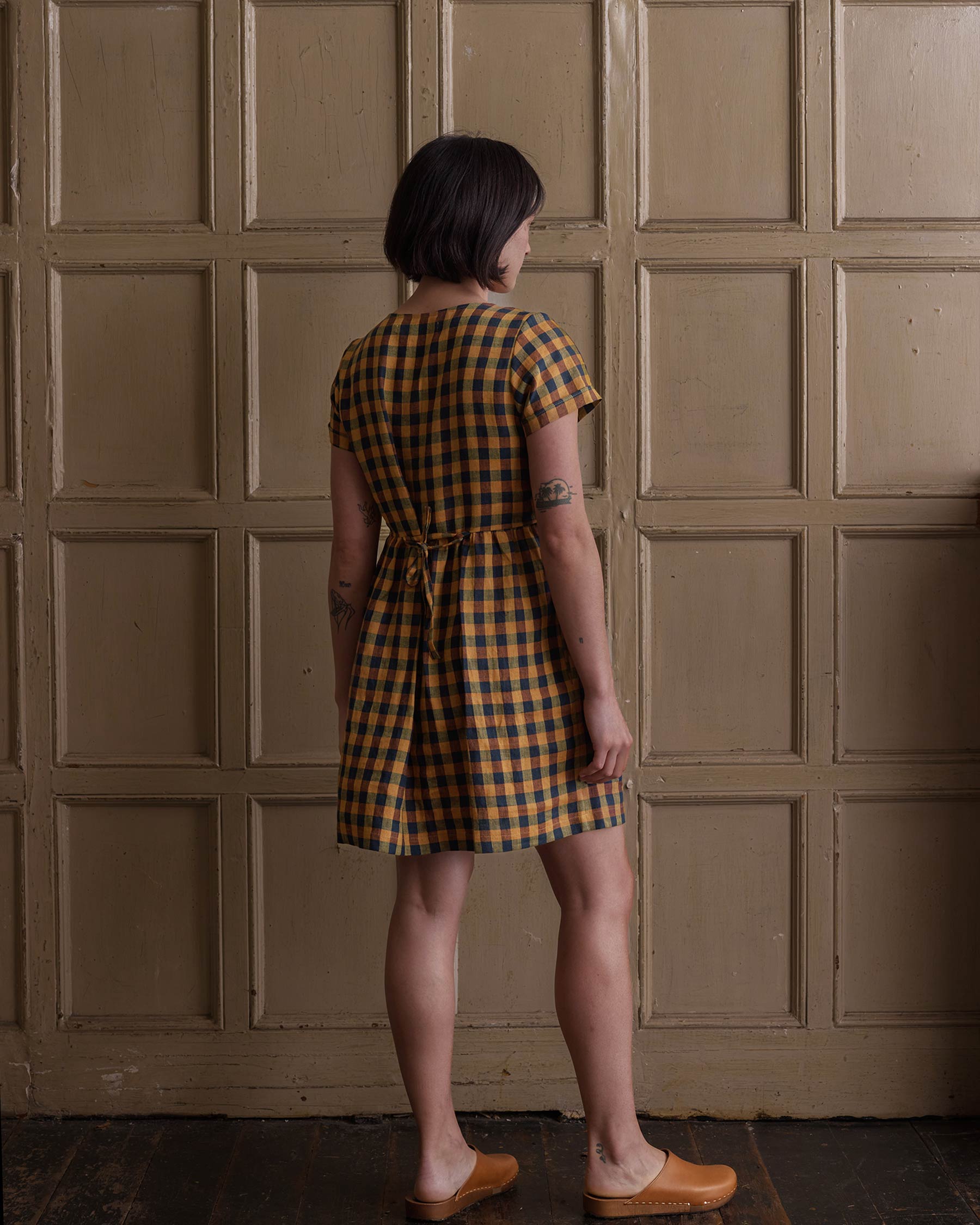 Back view of model wearing linen knee length dress in Basque Check, showing adjustable waist tie