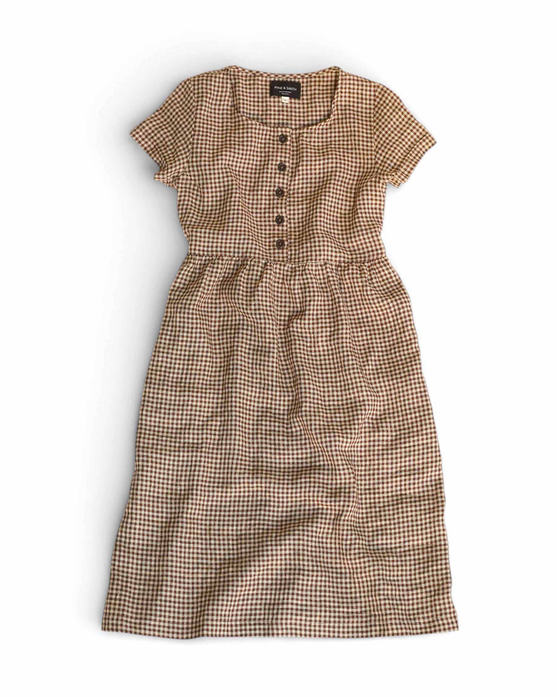 The No.11 Classic Button Up Linen Dress in Topsham Check by Pyne and Smith Clothiers is a short-sleeved, ankle-length European flax linen dress with brown and white checks, button front, and a gathered waist, laid flat on a white background.