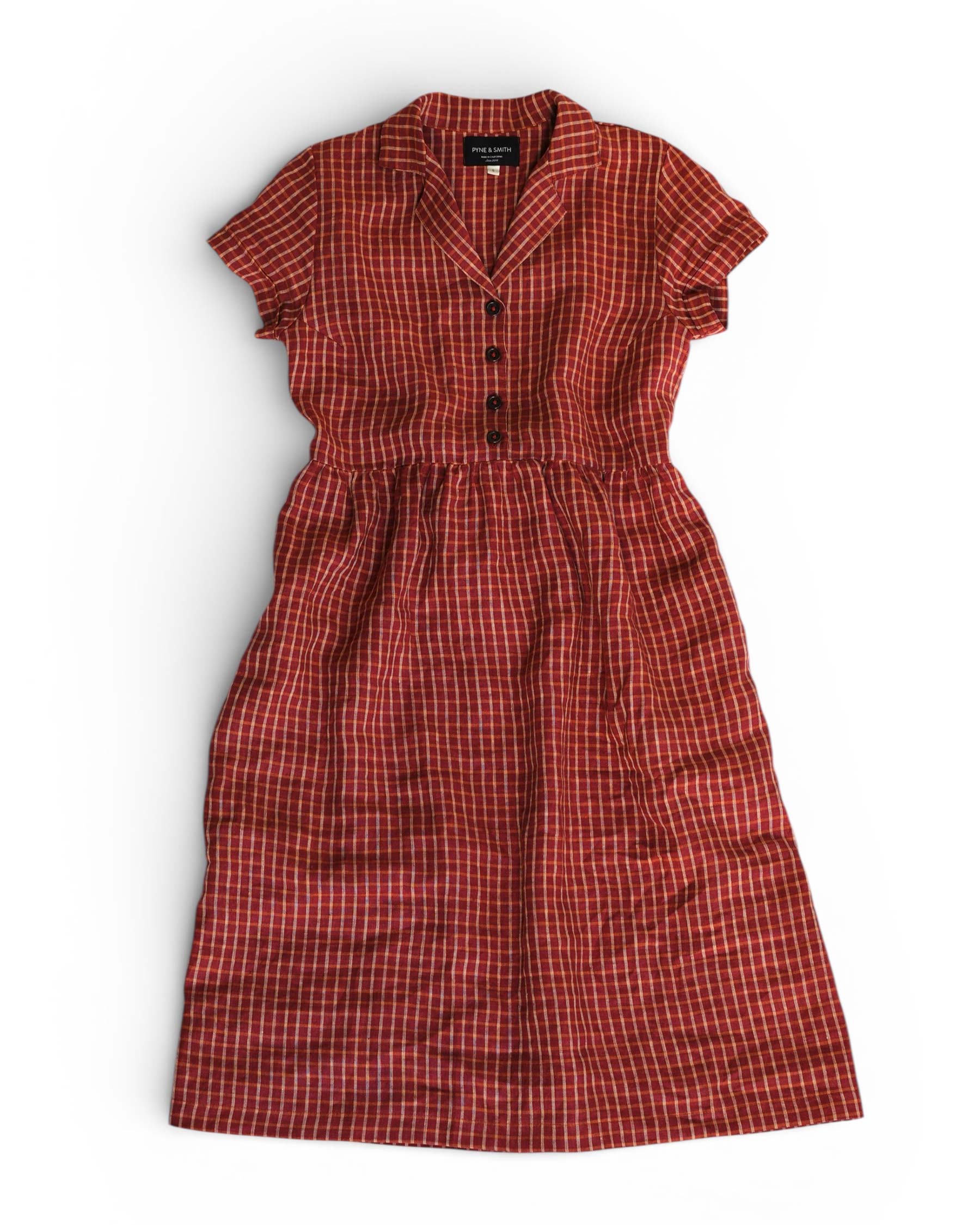 The No.30 Collared Linen Dress in Pomodoro Plaid by Pyne and Smith Clothiers is a vintage-inspired red, short-sleeved button-up with a gathered waist and white/black plaid pattern, shown laid flat on a white background.