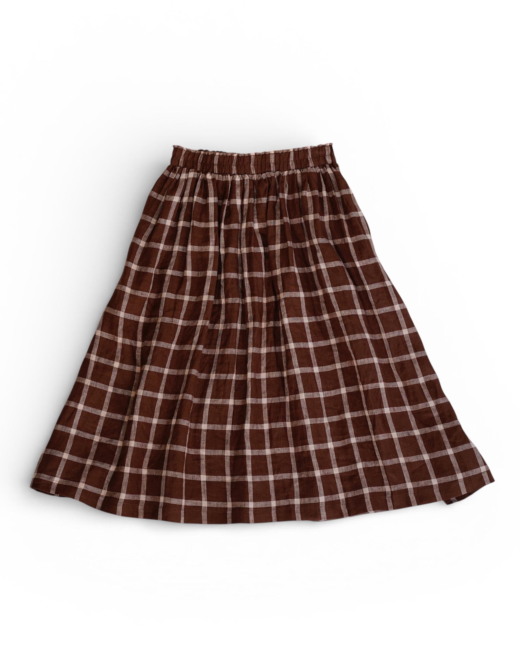 The Linen Skirt No.11 in Neapolitan by Pyne and Smith Clothiers is a brown checkered European flax linen skirt with an elastic waistband, featuring white and light brown plaid lines, shown laid flat on a white background.