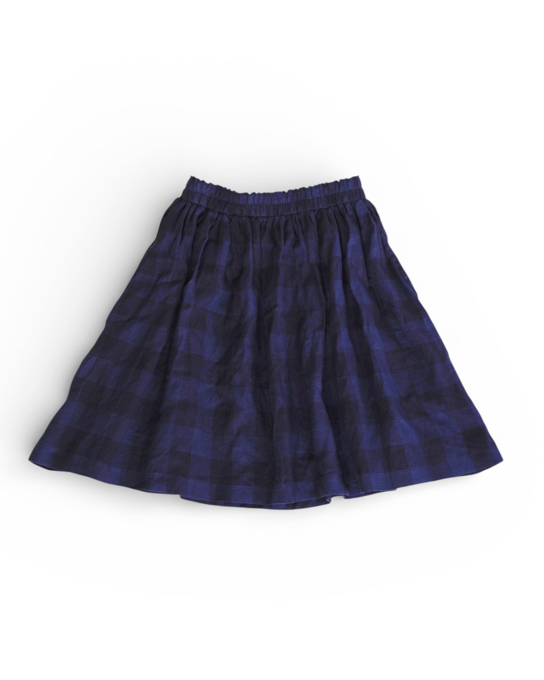 The Linen Skirt No.14 in Midsommar Night Check by Pyne and Smith Clothiers, a knee-length skirt with an elastic waistband and navy blue and black plaid pattern, is laid flat on a white background.