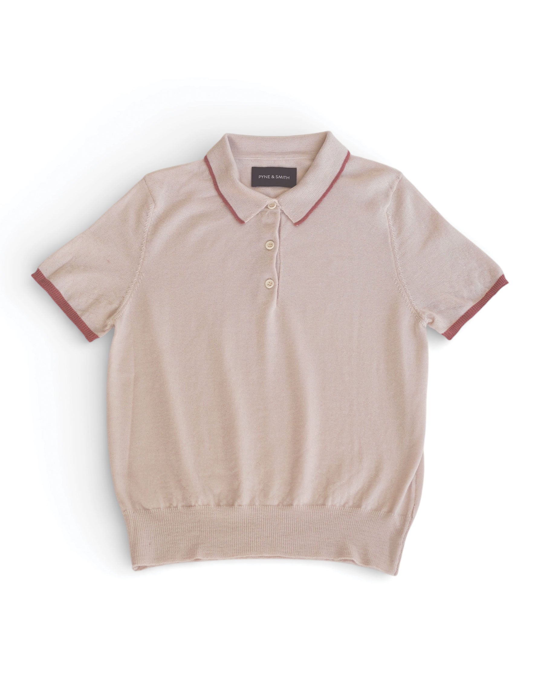 The Merino Polo Shirt in Shell Pink by Pyne and Smith Clothiers is a slim fit polo crafted from extra fine merino wool, with a three-button collar and muted red trim on the sleeves and collar, shown laid flat on a white background.